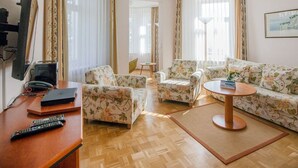 A hotel room with a wooden floor, floral-patterned sofas, a round coffee table, and a flat-screen TV on a wooden stand. - Apartment with sea view and 1 bedroom (Ostseebad Binz)