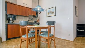 A dining area with a wooden table and chairs, a hanging light fixture, and a kitchen in the background. - Apartment with sea view and 1 bedroom (Ostseebad Binz)
