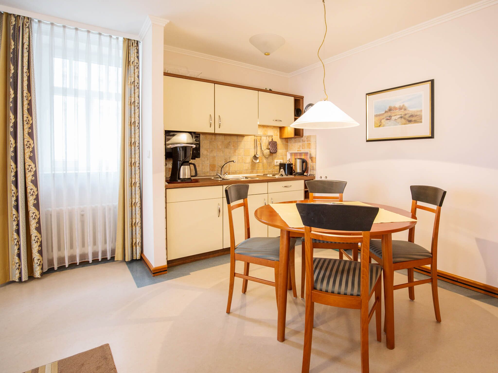 A modern kitchen with a dining area, featuring a round table, four chairs, and a pendant light.