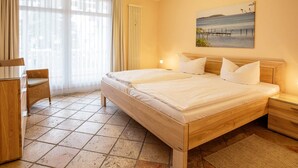 Ein Hotelzimmer mit einem großen Bett, einem Schreibtisch und einem Stuhl. An der Wand hängt ein Bild und es gibt ein Fenster mit Vorhängen.