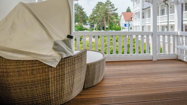 Eine überdachte Veranda mit Korbmöbeln und Blick auf Gebäude im Hintergrund.