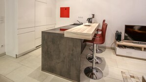 Una cocina moderna con una isla central, taburetes rojos, un televisor y una pared de acento roja.