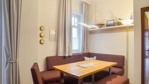 Una habitación con una mesa de madera y cuatro sillas tapizadas en rojo, un pequeño banco, una lámpara de pie y una ventana con cortinas.