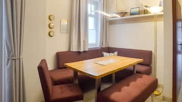 A room with a wooden table and four red upholstered chairs, a small bench, a floor lamp, and a window with curtains.