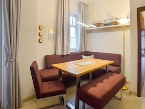 Ein Zimmer mit einem Holztisch, vier rot gepolsterten Stühlen, einer kleinen Bank, einer Stehlampe und einem mit Vorhängen versehenen Fenster.