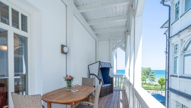 Una terraza de madera con muebles de mimbre, una mesa con un jarrón de flores y vista al mar.