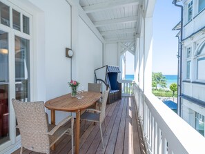 A wooden deck with wicker furniture, a table with a vase of flowers, and a view of the sea.