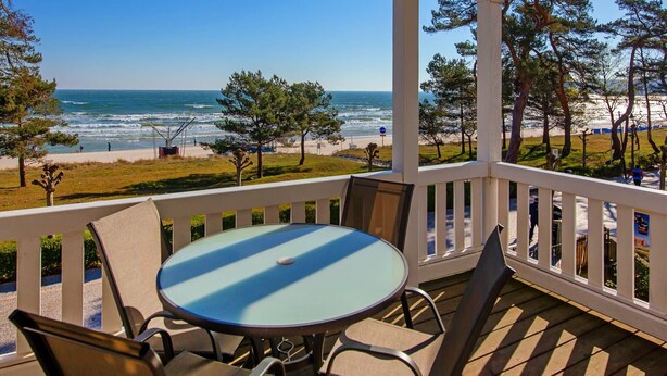 Un espace extérieur abrité, doté d’une table et de chaises, offrant une vue sur une plage et l’océan.