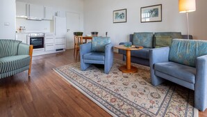 Un salon moderne comprenant un canapé, deux fauteuils, une table basse et un coin cuisine avec des placards et un four.