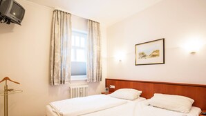 Une chambre d’hôtel avec deux lits, un radiateur, une télévision, un tableau encadré et une table de chevet.