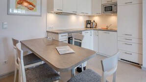 Une cuisine moderne avec des meubles blancs, un four à micro-ondes et une machine à café. On y trouve une table à manger avec deux chaises et un tableau encadré au mur.