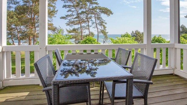 Un espace extérieur abrité, doté d’une table et de chaises, offrant une vue panoramique sur une forêt et l’océan.