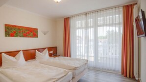 A hotel room with two beds, a painting on the wall, a window with sheer curtains, and a television on the wall. - Apartment with sea view, 2 bedrooms and balcony (Ostseebad Binz)