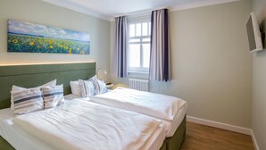 Une chambre d’hôtel avec deux lits, un tableau représentant un champ, une fenêtre avec des rideaux et un téléviseur à écran plat.