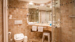 Une salle de bain avec une douche à parois de verre, des toilettes, un lavabo avec un miroir et un petit tabouret.