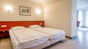 Ein Hotelzimmer mit Doppelbett, Nachttisch, einem gerahmten Bild an der Wand und Blick ins Freie durch ein Fenster.