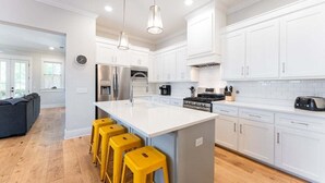 A modern kitchen with white cabinets, a central island with bar stools, stainless steel appliances, and pendant lighting.