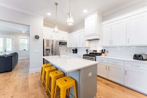 A modern kitchen with white cabinets, a central island with bar stools, stainless steel appliances, and pendant lighting.