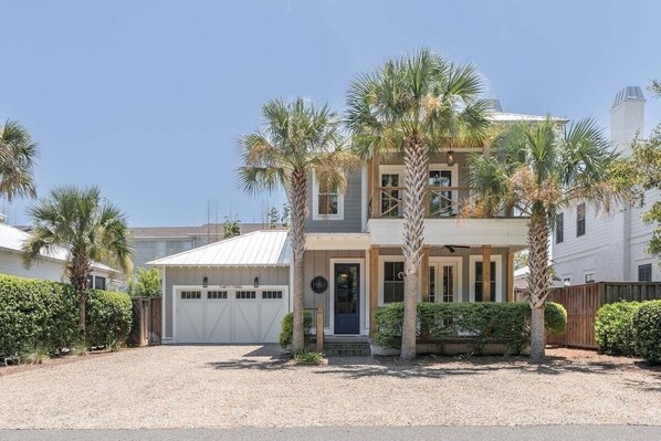A two-story house with a garage, palm trees, and a clear sky.