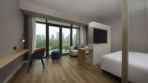 Ein modernes Hotelzimmer mit großem Fenster, einem Bett, einem Schreibtisch und einem Sessel.