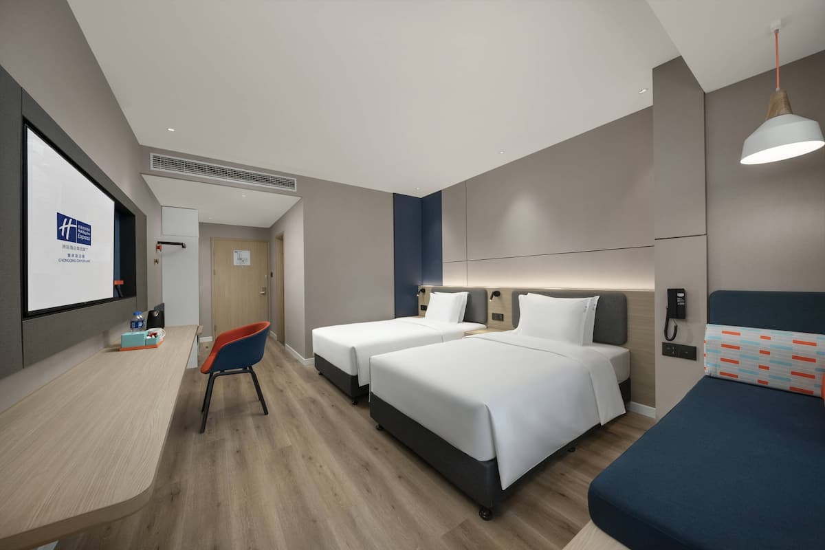 Una habitación de hotel con dos camas, un escritorio, una silla y una pantalla de televisión.