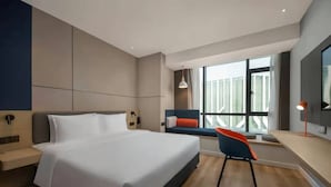 Ein modernes Hotelzimmer mit einem großen Bett, einem Schreibtisch mit Stuhl, einem Fenster mit Blick und einer kleinen Sitzecke mit Bank und Kissen.