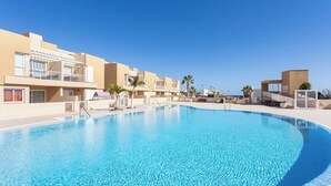 A swimming pool surrounded by modern buildings with balconies, clear skies, and palm trees. - Home2Book Stunning Sea Views El Porís (Porís de Abona)