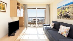 A modern living room with a flat-screen TV, a sofa with floral cushions, a dining area with a table and chairs, and a balcony with a view of the sea. - Home2Book Stunning Sea Views El Porís (Porís de Abona)
