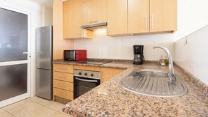 A compact kitchen with a refrigerator, microwave, stove, sink, and wooden cabinets. - Home2Book Stunning Sea Views El Porís (Porís de Abona)