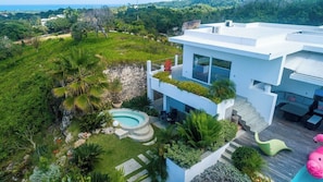 Una casa moderna de dos pisos con piscina, rodeada de exuberante vegetación y vista al océano.