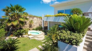 Una casa moderna con piscina, abundante vegetación y un muro de piedra.