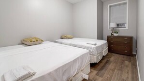 A bedroom with two beds, a dresser, and a window with blinds.