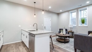 A modern kitchen with a built-in dishwasher, a dining area with a round table, and a gray sofa.