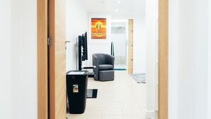 Un hall d’hôtel moderne avec une porte en bois, une poubelle noire, un fauteuil gris et un tableau encadré au mur.