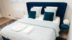 Une chambre à coucher avec une tête de lit capitonnée, une couvre-lit à motifs et des serviettes soigneusement pliées sur le lit.