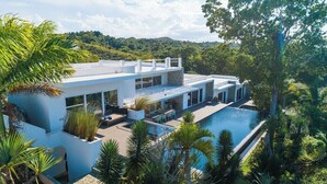Una casa moderna con piscina, rodeada de exuberante vegetación y colinas.