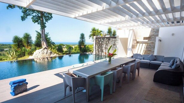 Un área junto a la piscina con mesa y sillas, un sofá y vistas al océano.