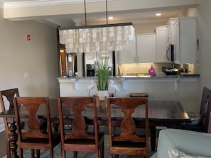 A dining area with wooden chairs, a central table, and a kitchen in the background.