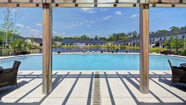 Un espace piscine agrémenté d’une pergola, de chaises longues et offrant une vue sur les immeubles d’habitation en arrière-plan.