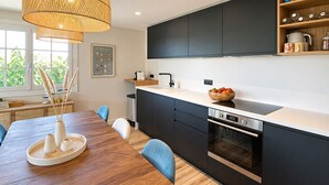 Een moderne keuken met donkere kastjes, een wit aanrechtblad, een groot kookeiland met zitplaatsen en een hangende lamp.