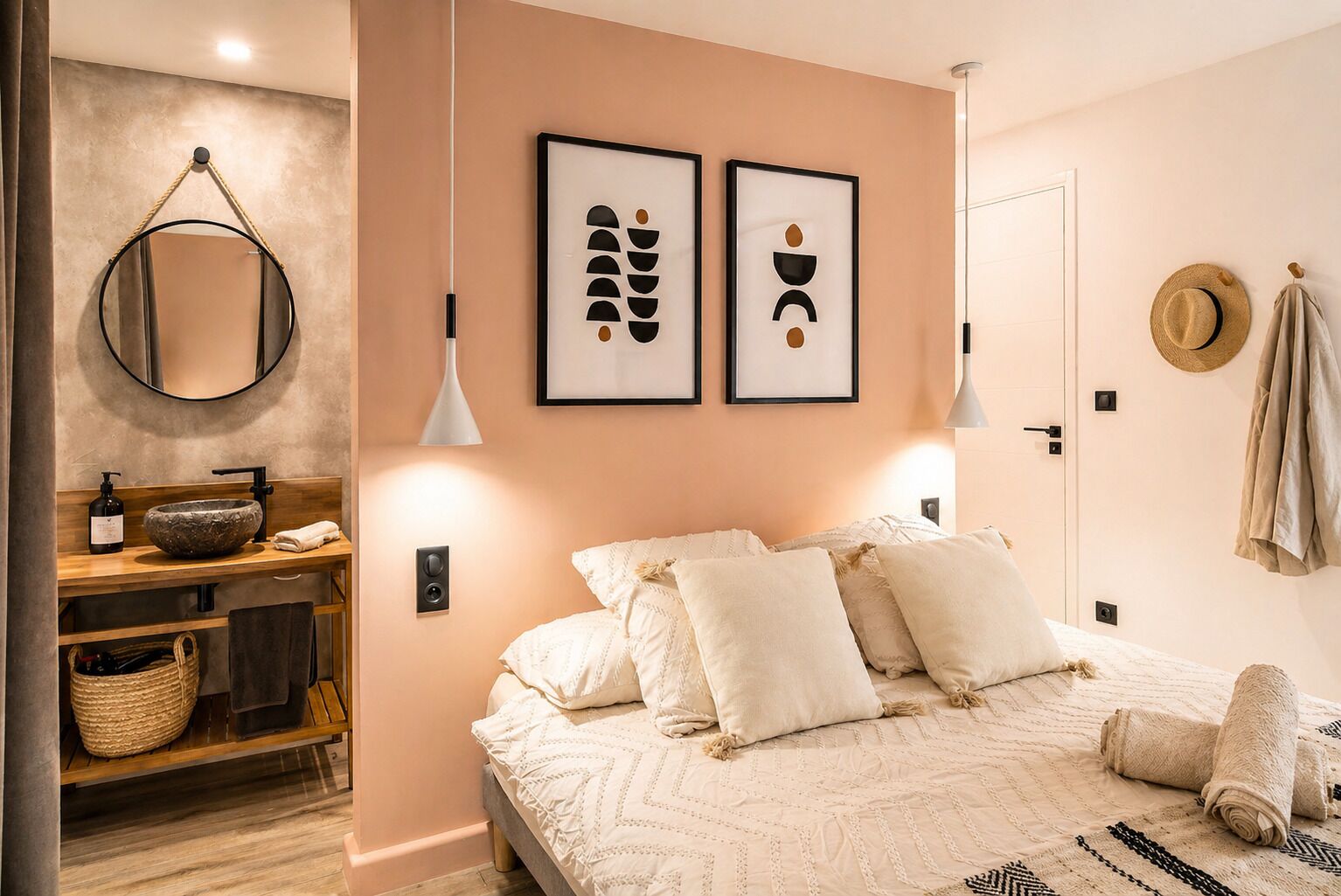 A bedroom with a bed, pillows, a bedside table, a mirror, framed artwork, and a hat on the wall.