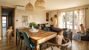 Een moderne woonkamer met een houten eettafel, blauwe stoelen, een donkere bank en een groot raam met gordijnen.