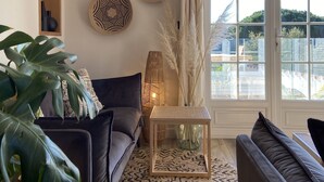 Een woonkamer met een donkere bank, een ronde salontafel en een grote plant.