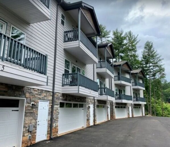Un immeuble résidentiel à plusieurs étages, doté de balcons, d’une façade en pierre et d’une allée menant à un espace de stationnement.