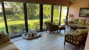 A spacious living room with a large sliding glass door leading to a garden, furnished with a sofa, chairs, and a pet bed. - Sarasota 3 bedroom villa conveniently located on Palm Aire Golf Course community (Sarasota)