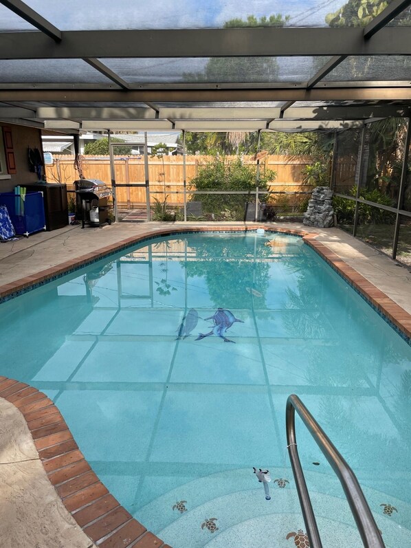 Una piscina con cerramiento de vidrio, un muelle de madera y una zona de barbacoa.
