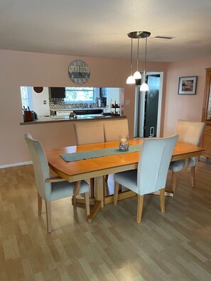 Un área de comedor con una mesa de madera y sillas azul claro, una lámpara colgante y vista a la cocina.