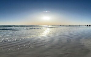 Una playa con cielo despejado y el sol bajo en el horizonte.