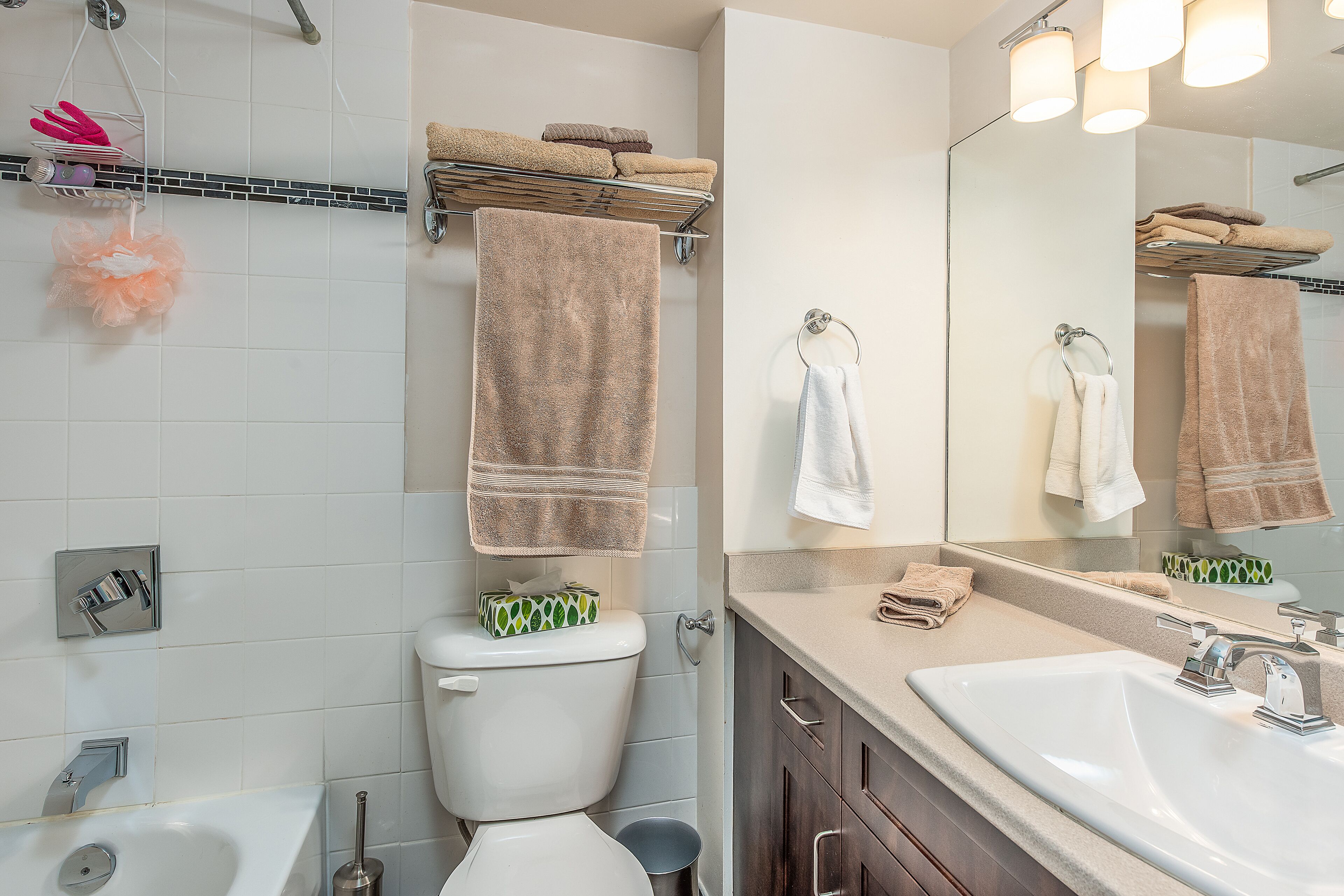 Une salle de bain moderne avec un lavabo blanc, un miroir et des toilettes. On aperçoit des serviettes sur un porte-serviettes et une tringle à rideau de douche au-dessus de la douche.