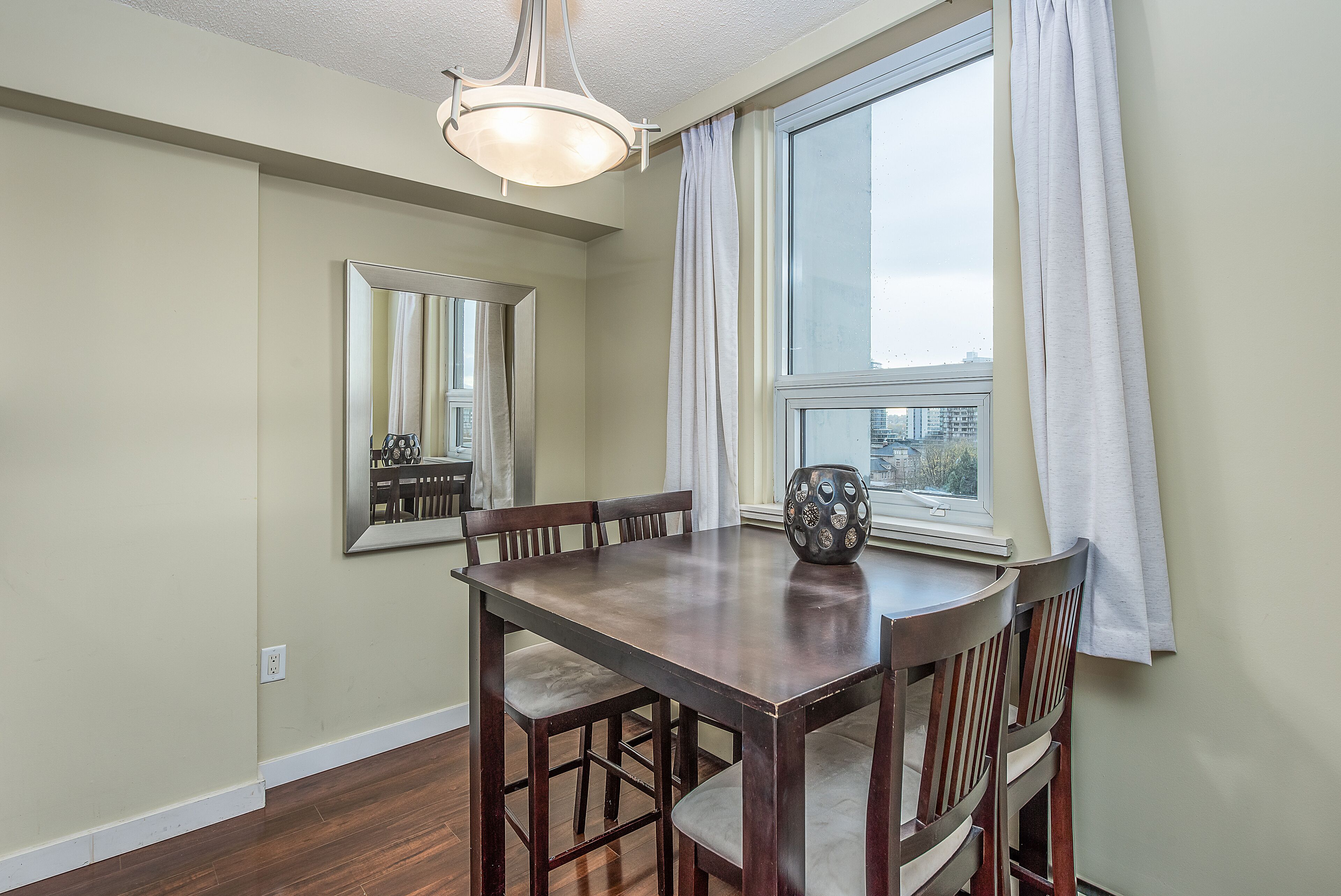 A dining area with a wooden table and chairs, a large mirror, and a window with curtains.